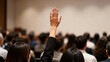 © Robert Garcia - Close-up of a participant's hand raised, asking a question or voting during a professional conference or seminar, highlighting active engagement and communication.
