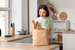 © Pixel-Shot - Young Asian woman with shopping bag full of fresh food at table in kitchen