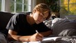 © Ireen - A teenager writing poetry in a diary, lying on a couch with soft sunlight streaming through a window.