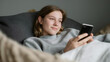 © Smejanka - Smiling teenage girl using a smartphone while relaxing on a couch at home