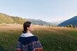 © SHOTPRIME STUDIO - Woman stands in meadow valley looking at mountains and nature landscape outdoors, travel portrait in sweater with serene scenery, grass, sky and panoramic alpine view.