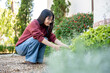 © bongkarn - Glasses asian woman in sweater looking and touching flowers while crouching sitting in garden cafe.
