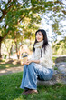 © bongkarn - Asian woman in sweater and scarf holding coffee and warming hands as sitting on rock in garden park.