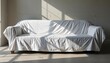 © Cherrin - A covered couch in a sunlit room with a minimalist aesthetic.