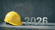 © julijadmi - Yellow hard hat beside metallic numbers 2026 on textured concrete surface, symbolizing new beginnings and construction themes for the upcoming year