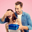 © vgstudio - Holiday sales, price discounts, celebrating ad concept - happy smiling man covering expressive surprised woman eyes while holding blue gift box. Isolated rose pink background. Square