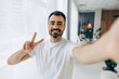© Maria Vitkovska - Happy handsome man taking selfie showing peace sign indoors