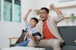 © itchaznong - Family Life: Father and son celebrating a gaming victory at home