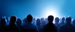 © perfectlab - Silhouettes of diverse audience members watching a bright stage or screen in a darkened room with blue ambient lighting