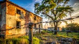 Rusty barbed wire fence in front of old brick building at sunset