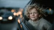 © Pinklife - A cheerful young boy with curly hair peering out of a car window, showcasing a sense of freedom and joy against a backdrop of moving city lights during twilight.