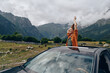 © SHOTPRIME STUDIO - roadtrip travel woman mountains car nature inclusivity authenticity joyful woman standing through car sunroof on countryside road with mountains celebrating adventure and freedom in authentic moment
