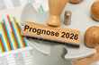 © Wolfilser - Ein Holzstempel ist beschriftet mit dem Aufdruck Prognose 2026 als Symbolbild für die Vorhersage einer Entwicklung in Wirtschaft, Industrie oder Gesellschaft für das Jahr 2026 - digital bearbeitet
