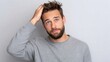 © SerPak - A young man with a beard and casual attire looks puzzled while scratching his head. The setting is neutral and minimalistic, conveying a sense of uncertainty.