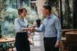 © qunica.com - A man and a woman in smart casual attire share a handshake on a sunny urban street, signaling trust, collaboration, and a positive business connection.