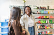 © Koldo_Studio - Two young women engaging in positive conversation while browsing products, choosing items in a modern drugstore or beauty store