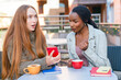 © Iryna - Friends sharing exciting news while sitting at a cafe table in a lively outdoor setting