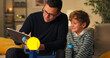 © ABCreative - Son is spending time with dad men are sitting on couch playing with a model of planetary system guy is explaining to boy about construction of cosmos using toy as example he is naming planets.
