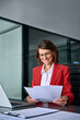 © Stock 4 You - Smiling European Latin business woman accountant analyst holding documents, work at laptop computer doing online trade market tech research. Hispanic businesswoman with paperwork in office. Vertical