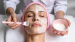 © SIDDQUE  - Woman receiving facial mask application with brush and bowl.