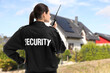 © New Africa - Security guard in uniform using radio near house outdoors, back view. Private property protection