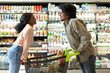 © Prostock-studio - Two individuals playfully engage while pushing a shopping cart filled with groceries in a well-stocked supermarket. Their smiles create a warm atmosphere during their shopping trip.