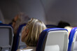 © Laurentiu Bratu - close-up back view of a blonde female passenger with sunglasses resting on her head, seated in an economy class airplane seat in the dark cabin during a flight