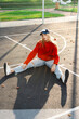 © Sergey Narevskih/Stocksy - Woman sitting on outdoor basketball court in red sweatshirt
