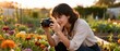 © Rahmatsapp - A young woman with a camera captures the vibrant beauty of colorful flowers in a sunny outdoor garden.