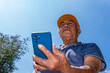 © NAILOTL MENDEZ/Stocksy - Mexican elderly man using mobile phone outdoors under blue sky
