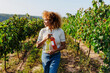 © BONNINSTUDIO/Stocksy - Woman carrying wine bottles walking through vineyard