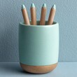 © A4719 - A close up studio shot of four wooden pencils with mint green tips contained within a speckled mint green ceramic holder with a wooden base, resting on a textured gray surface.