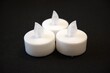 © Veronika - 3 white electric candles on a black background with Copy Space in natural condition.
