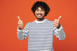 © ViDi Studio - Young smiling happy fun Indian man he wears striped sweatshirt casual clothes showing thumb up like gesture looking camera isolated on plain red orange background studio portrait. Lifestyle concept.