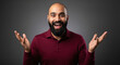 © PRASANNAPIX - A bald Indian man in a maroon polo shirt gestures with both hands raised in a questioning or expressive pose against a dark background.