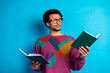 © deagreez - Young man in colorful sweater reading two books against vibrant blue background
