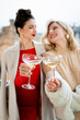 © Kristina89 - Two young women in festive dresses and with glasses of champagne in their hands celebrate the New Year and Christmas.