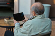 © master1305 - Senior man relaxing outdoors with tablet at patio table in peaceful mood. Concept of lifestyle leisure, senior technology use, home comfort scenes, and calm everyday moments.