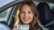 © Yurij - Young woman smiling inside a car holding a driver?s license while wearing a seatbelt, demonstrating safe driving and personal achievement on a bright day