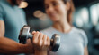 © Denis Yevtekhov - Fitness trainer guiding client through defocused dumbbell workout, faceless motivation session, sweat visualization detail, blurred gym background, focus concept, training interfac