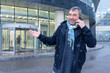 © lara-sh - Cheerful gesture as man holds phone beside contemporary facade with snowflakes falling over damp pavement in cold season