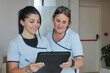 © atikinka2 - Two female healthcare workers reviewing information together on a black board, smiling and discussing their work in a clinical setting.