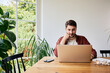 © baranq - Man using laptop at home sitting at dinning table working remotely