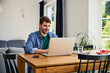 © baranq - Man working remotely from home on laptop at dinning table