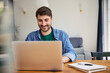 © baranq - Young men using laptop at home sitting at a table