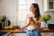 © baranq - Young woman enjoying morning coffee at home standing in a kitchen