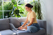 © baranq - Smiling young woman using laptop sitting on sofa at home
