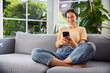 © baranq - Young woman sitting comfortable on sofa using mobile phone at home