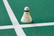 © Sophon_Nawit - A white shuttlecock sits perfectly on the intersection of the two white service lines, sharply contrasting with the deep green texture of the badminton court surface.