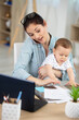 © auremar - mother holding baby while working in home office